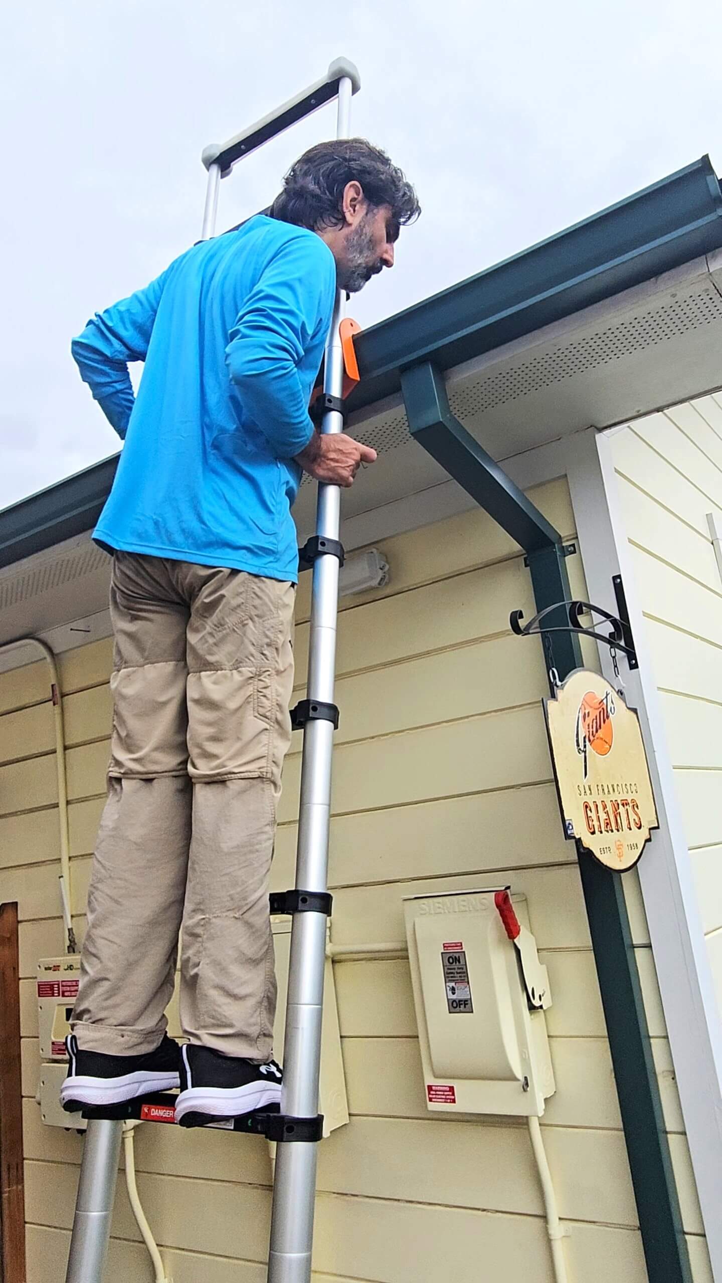 Man on ladder checking gutter downspout in Loomis, CA.