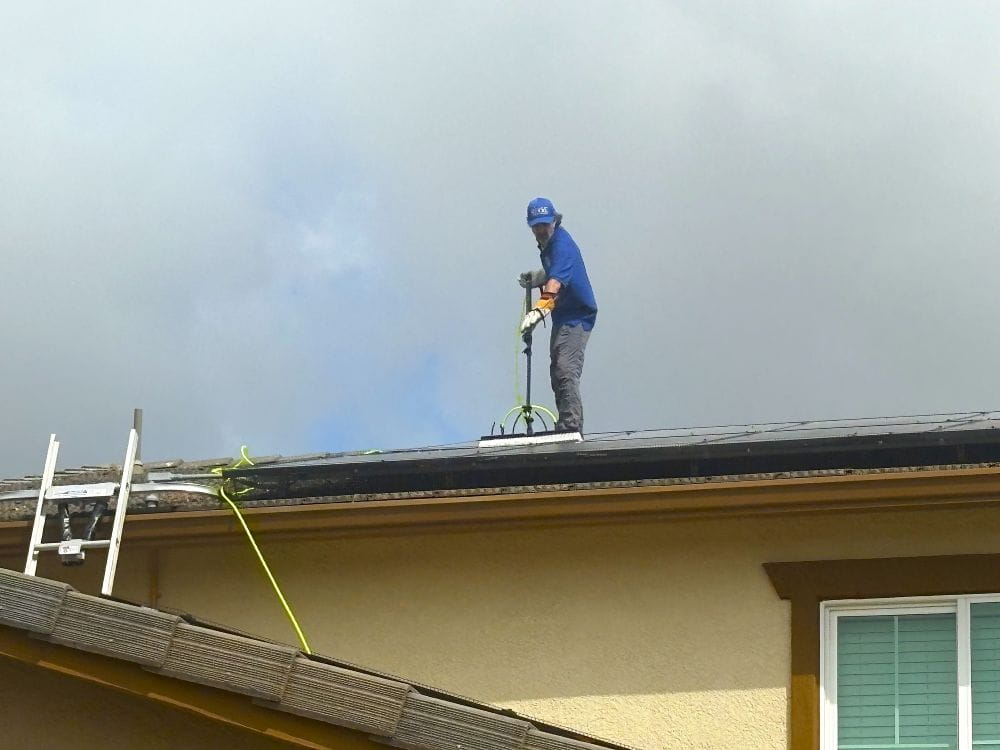 Man cleaning solar panels on second story roof with a water-fed brush.